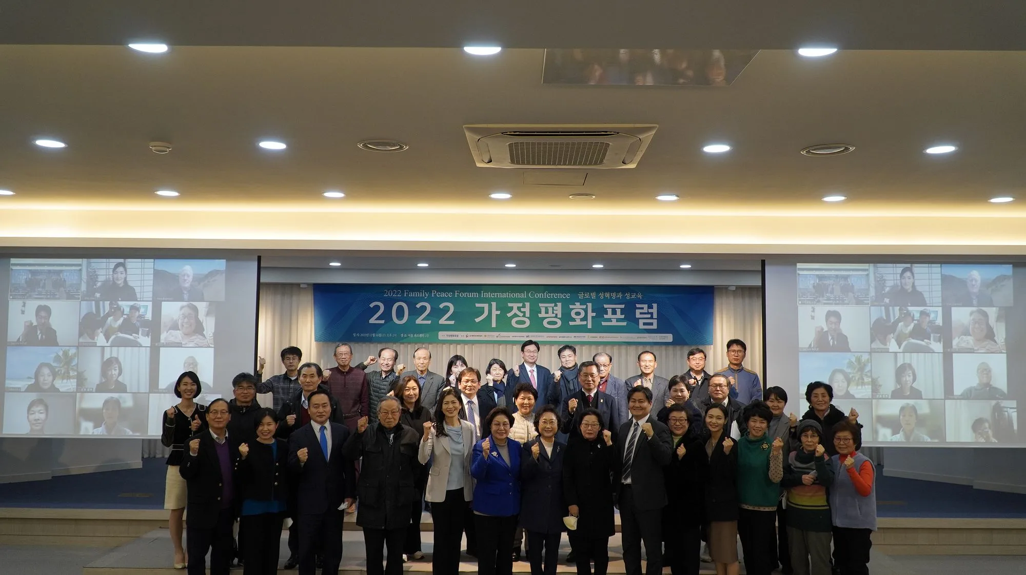 2022년 12월 제5회 국제가정평화포럼 '글로벌 성혁명과 성교육' 현수막 앞에 모인 참석자들과 좌우 화면의 화상 참여자들
