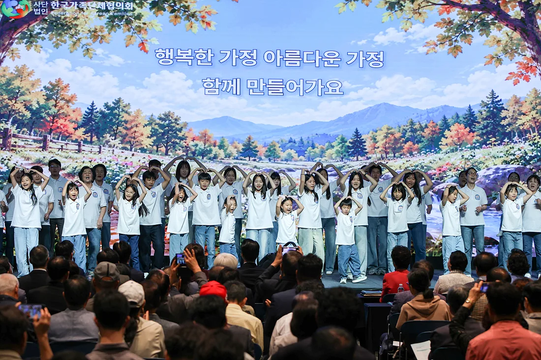 흰 티셔츠를 맞춰 입은 어린이와 가족들이 무대에서 머리 위로 하트를 그리며 합창하는 모습
