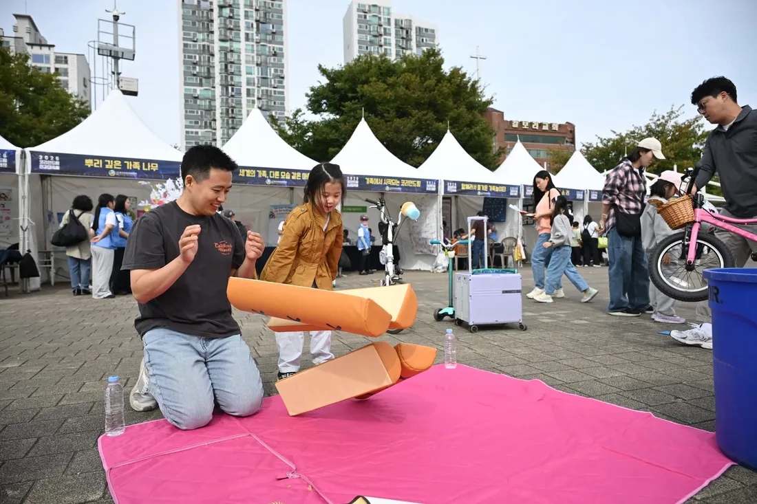분홍 돗자리 위에서 아버지와 딸이 전통놀이 도구를 가지고 함께 노는 모습