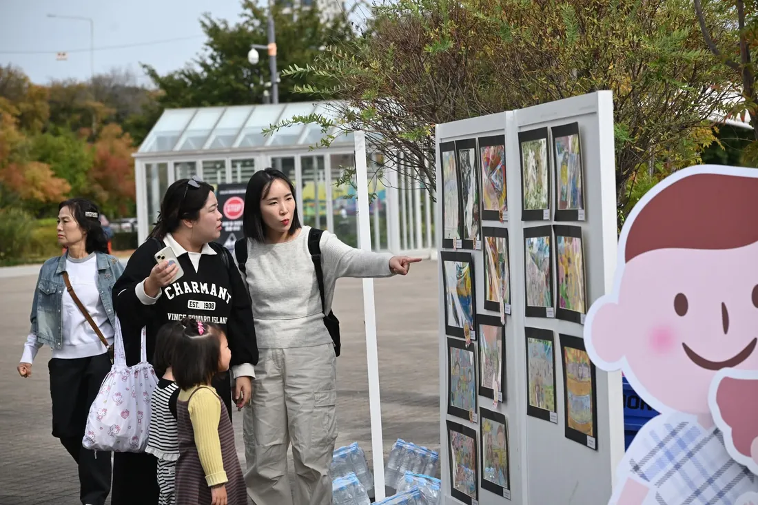 가족들이 전시판에 걸린 가족그림을 손으로 가리키며 살펴보는 모습