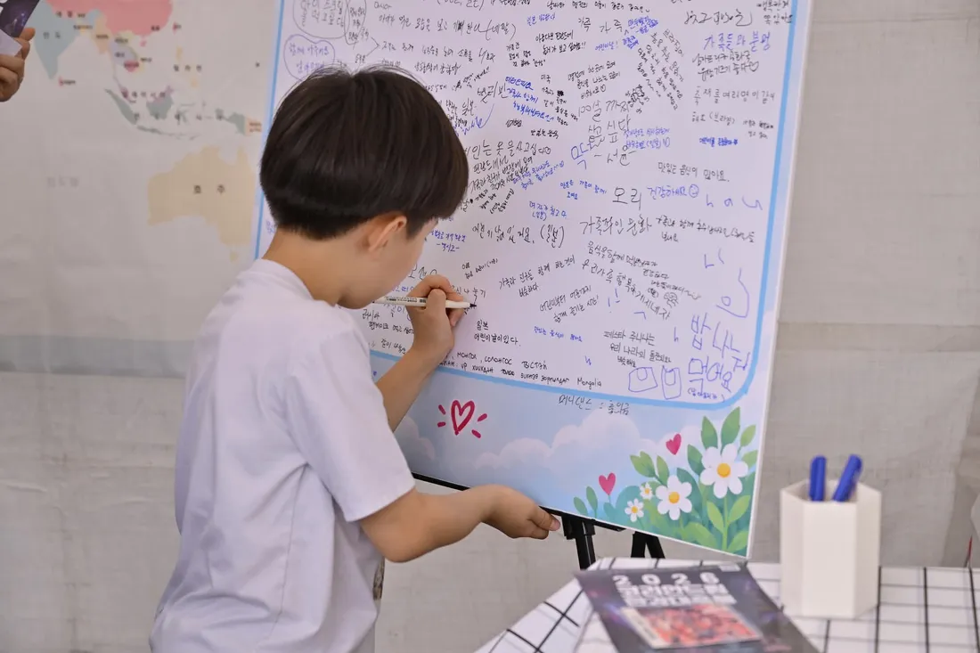 어린이가 세계 지도 옆 질문판에 세계 가족문화에 대한 생각을 적는 모습